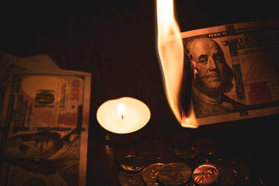 A dollar bill on fire above a burning candle